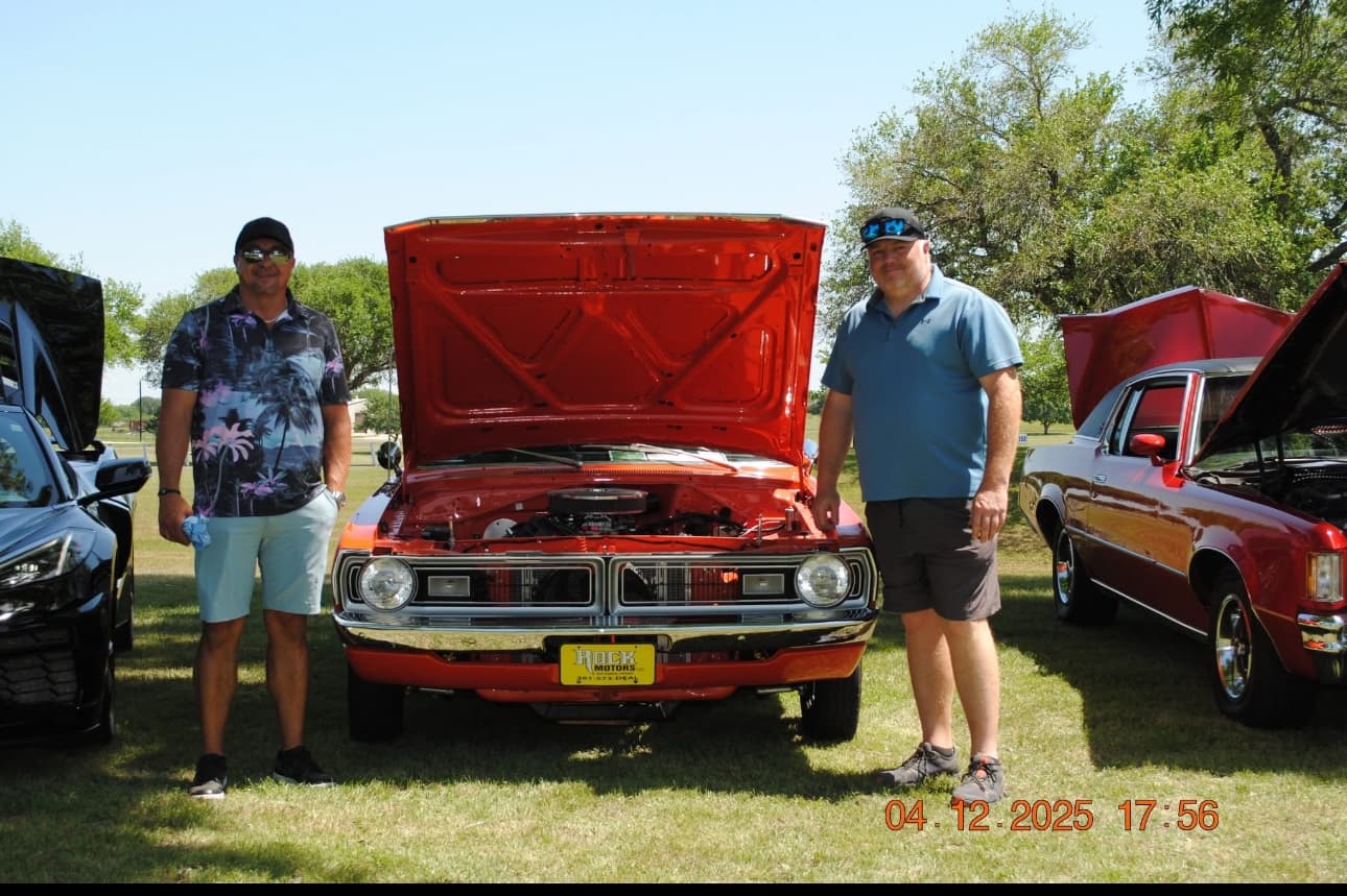 The founder and his cousin standing beside the cousin's orange Dodge Demon at a local car show